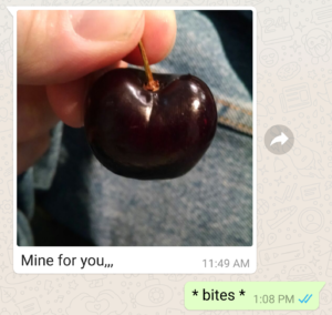 dark red cherry held between a man's fingers with a text message reading "Mine, for you"