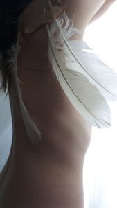 side view of woman's nude torso with feathered wings bandaged to her back
