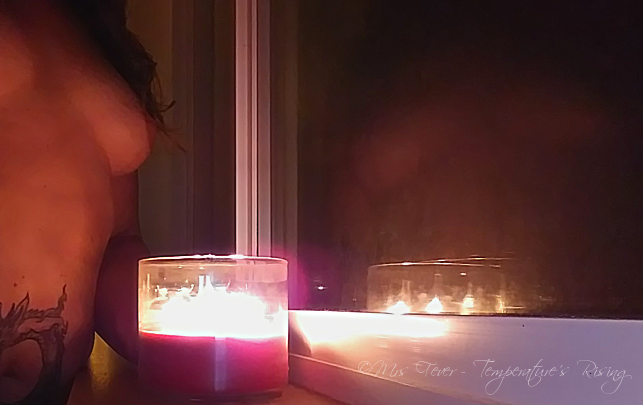 nude woman holding candle in front of window reflection
