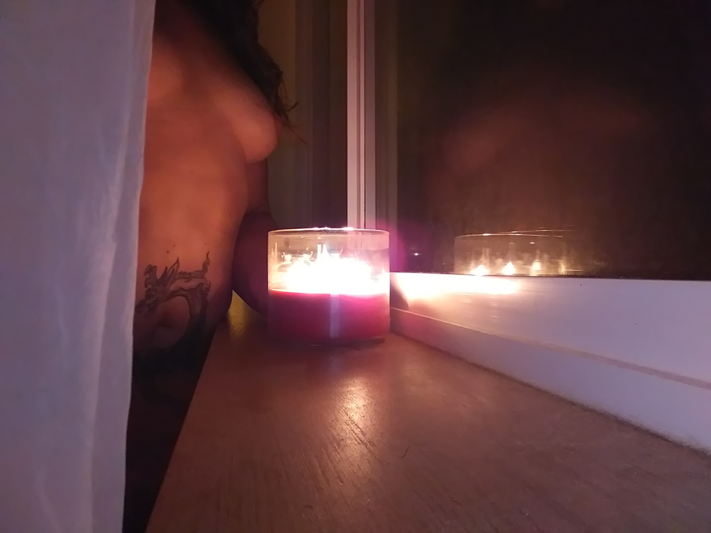 nude woman holding candle in front of window reflection
