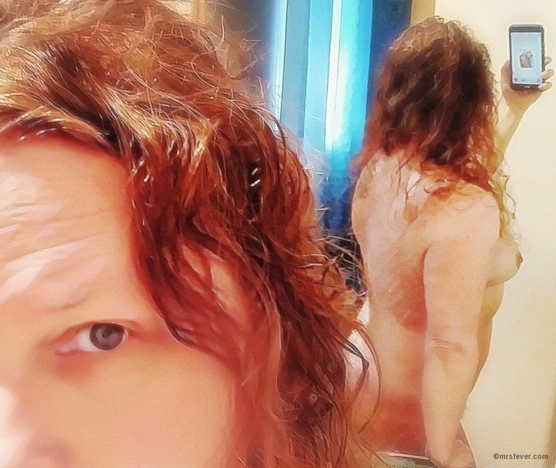 mirror photo showing woman's face in the foreground and side view of nude head and torso in background