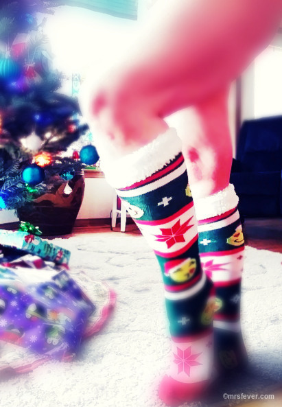 nude woman wearing Christmas socks standing knee-out next to Christmas tree