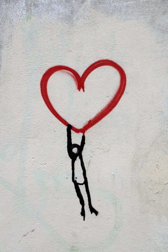 photo of ink on white wall showing stick figure person holding red heart, from Unsplash