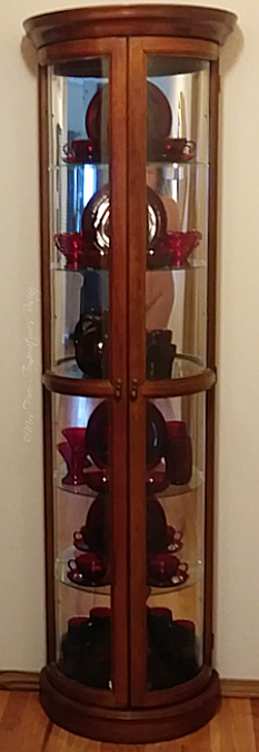 tall display case featuring ruby red depression glass with woman's nude figure reflected in mirror