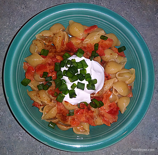 bowl of red pepper cheddar shells, topped with paprika and garnished with sour cream and chives