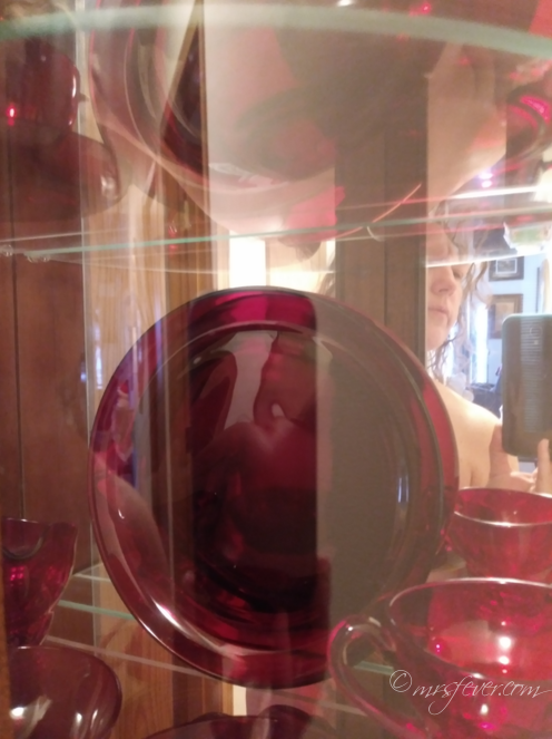 reflected light against a glass shelf holding ruby red depression glass forms the impression of a breast