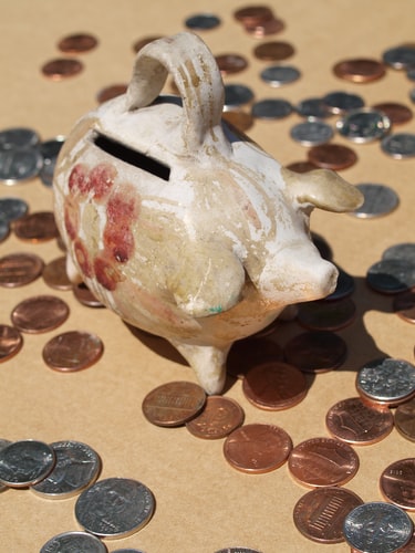 ceramic piggy bank on table surrounded by coins, viaDiane Helentjaris at Unsplash
