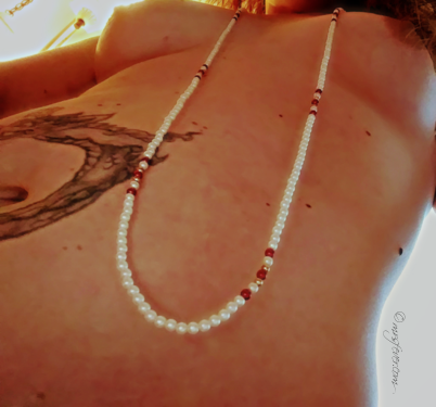 long swoosh of pearl-and-jewel strand necklace seen from upward view of woman's nude torso