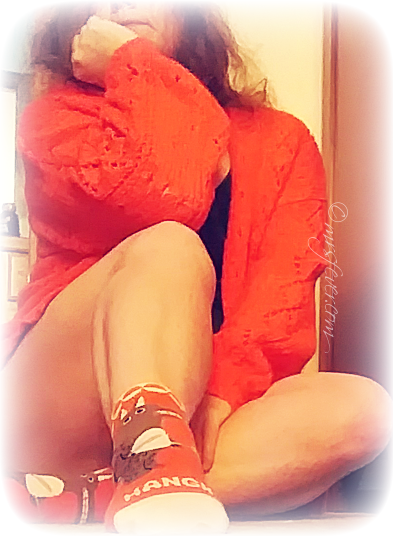 woman seated with elbow on knee and hand on chin, wearing orange sweater and HANGRY socks
