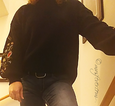 woman wearing belted jeans and black embroidered-sleeve sweater