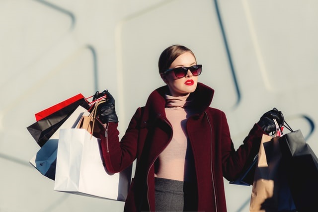 woman wearing dark coat and sunglasses holding several shopping bags in each hand -- image via Unsplash!