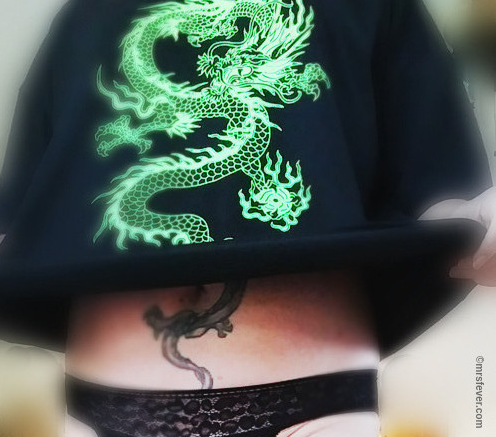 woman wearing black panties and holding up dragon T-shirt to reveal dragon tattoo underneath