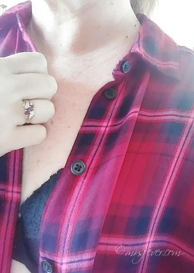 chest and shoulder shot of woman holding unbuttoned red plaid shirt, draped open to show a black bra