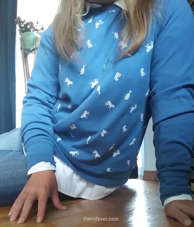 woman seated on wood floor wearing blue sweatshirt with small white tigers on the front
