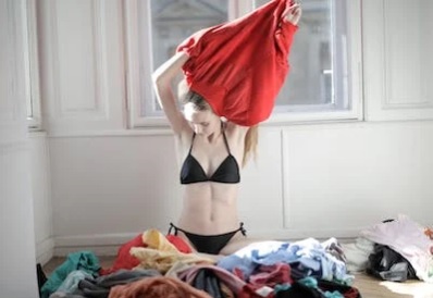 woman sitting on pile of clothes wearing underwear, trying on shirt