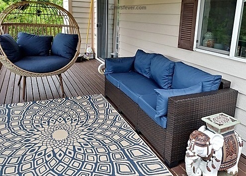 wicker deck couch and egg chair on brown deck boards with  blue & tan outdoor carpet and elephant side table